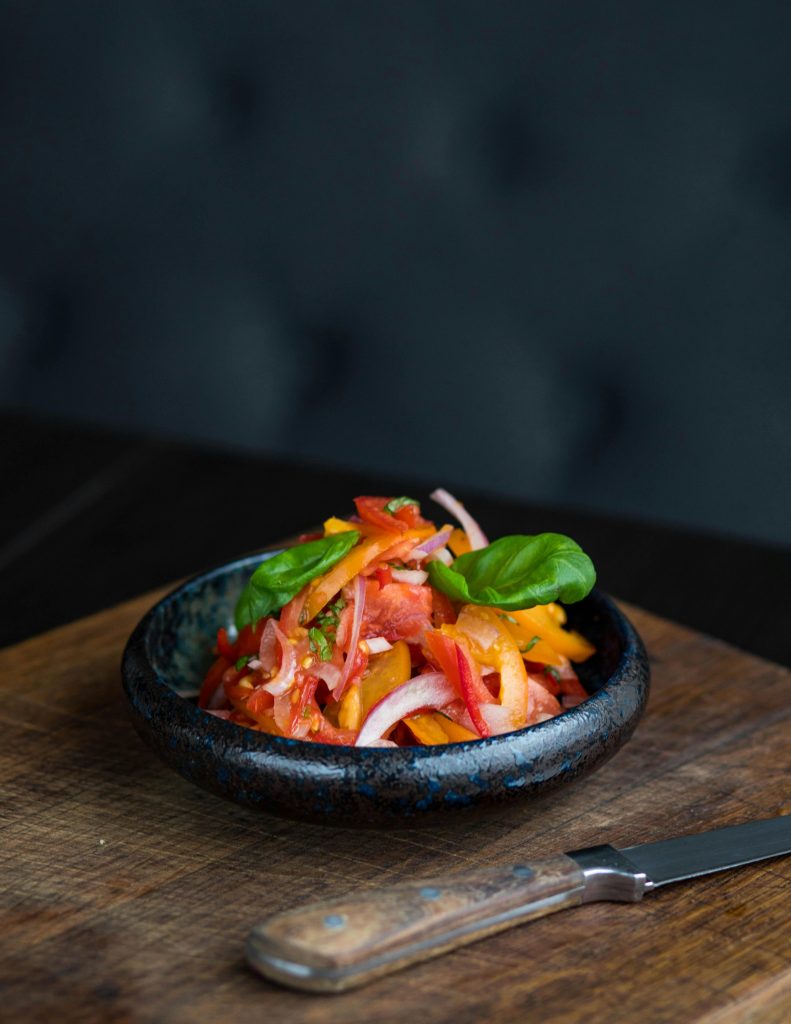 Fresh vegetable salad with colorful peppers and onions in a black bowl on a wooden board.