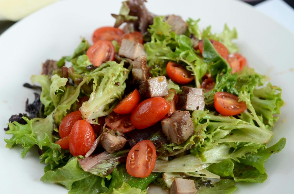 Delicious mixed greens with cherry tomatoes and meat served on a white plate, perfect for a healthy meal.